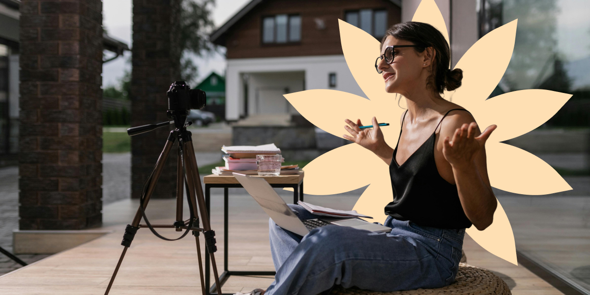 A woman sitting Turkish and with her arms spread in front of a camera with a laptop and notes on her lap explaining something